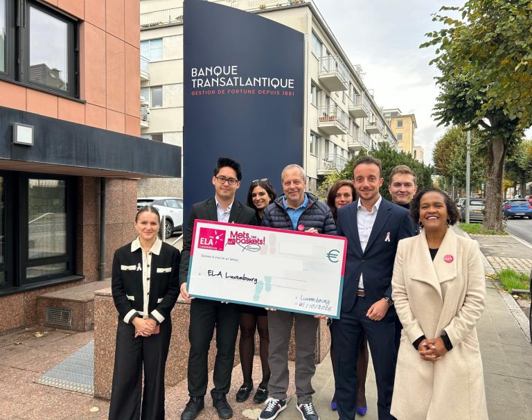 Des collaborateurs de la Banque Transatlantique Luxembourg et de l’équipe d’ELA posent avec le chèque « Mets tes baskets ! » devant l’immeuble de la banque