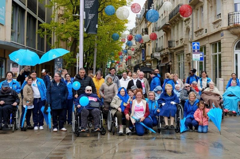 Résidents et équipes de Päiperléck rassemblés dans une rue, sous des parapluies bleus
