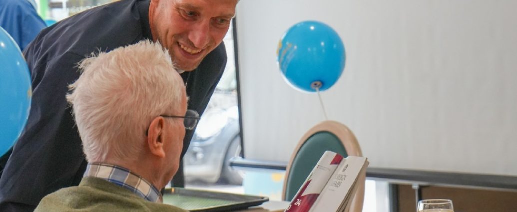 Jeff Strasser échange avec un résident de la résidence Bel-Âge, qui feuillette une brochure, lors de la journée Mets Tes Baskets du 13 mai 2026