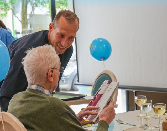 Jeff Strasser échange avec un résident de la résidence Bel-Âge, qui feuillette une brochure, lors de la journée Mets Tes Baskets du 13 mai 2026